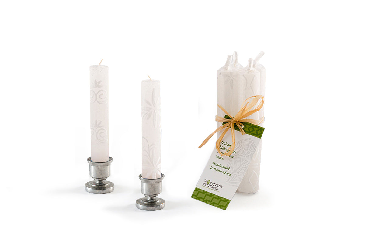 A pair of White on White Shabbat candles in pewter taper holders, with a pack of 4 tied together with a story card showing how these candles are sold in a gift pack.