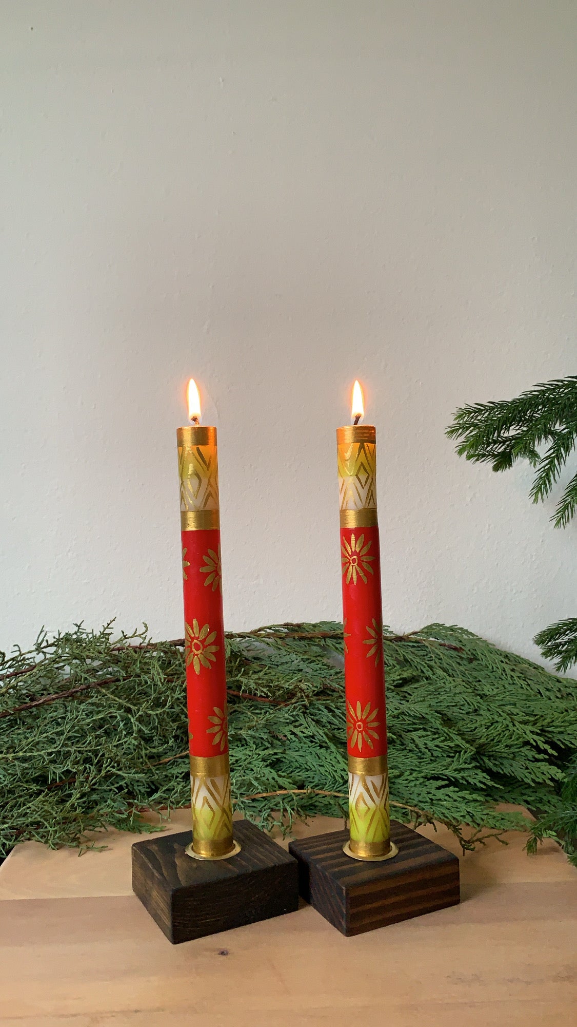 Christmas hand made and hand painted taper candle pair in dark brown taper candle holders. The taper candles are lite and are hand painted  red with gold designs. Fair Trade candles.