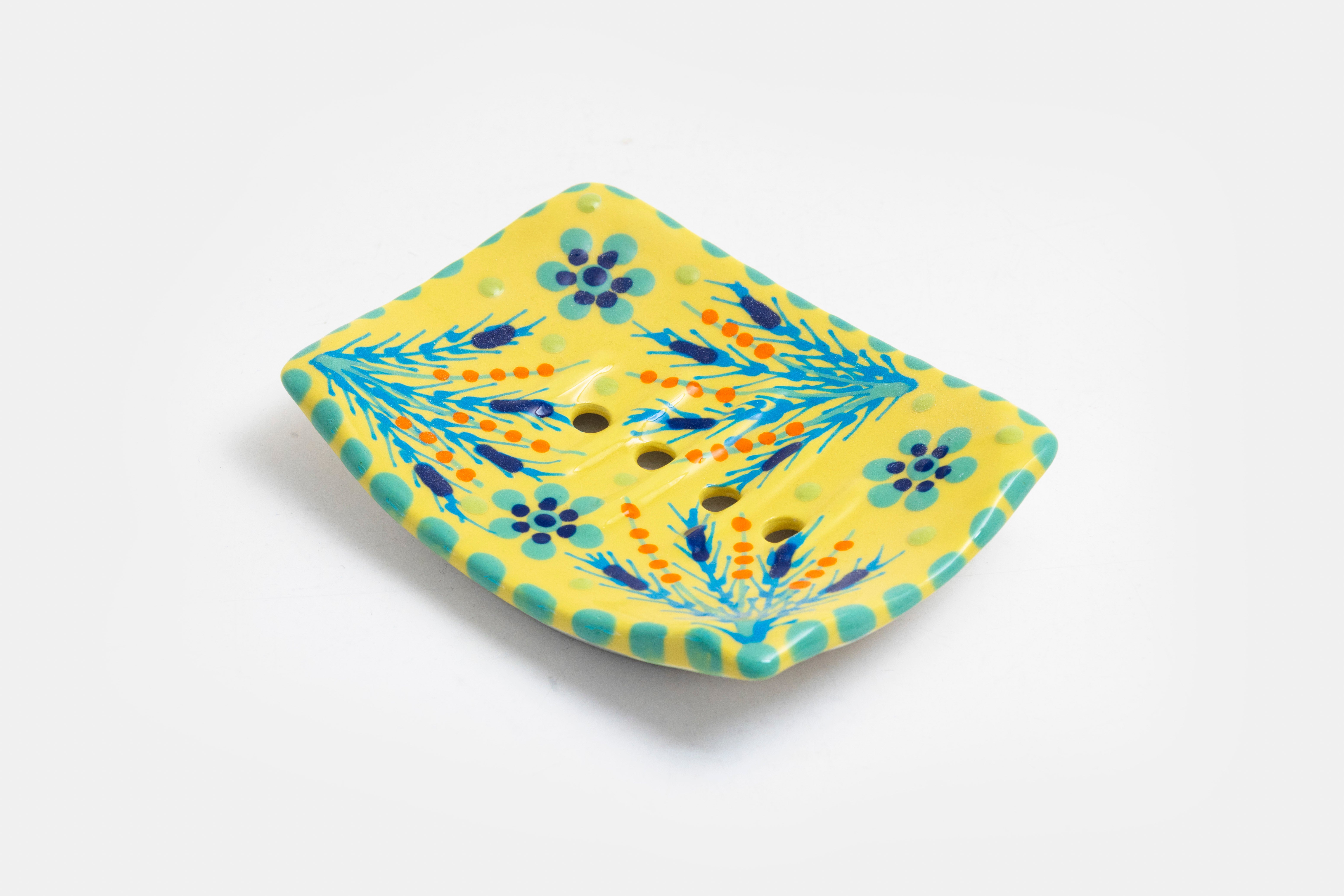 Ceramic square soap dish with base color of yellow. Flowery design with dots painted on top in jasper green, turquoise, red and touches of orange. Drain holes in dish!