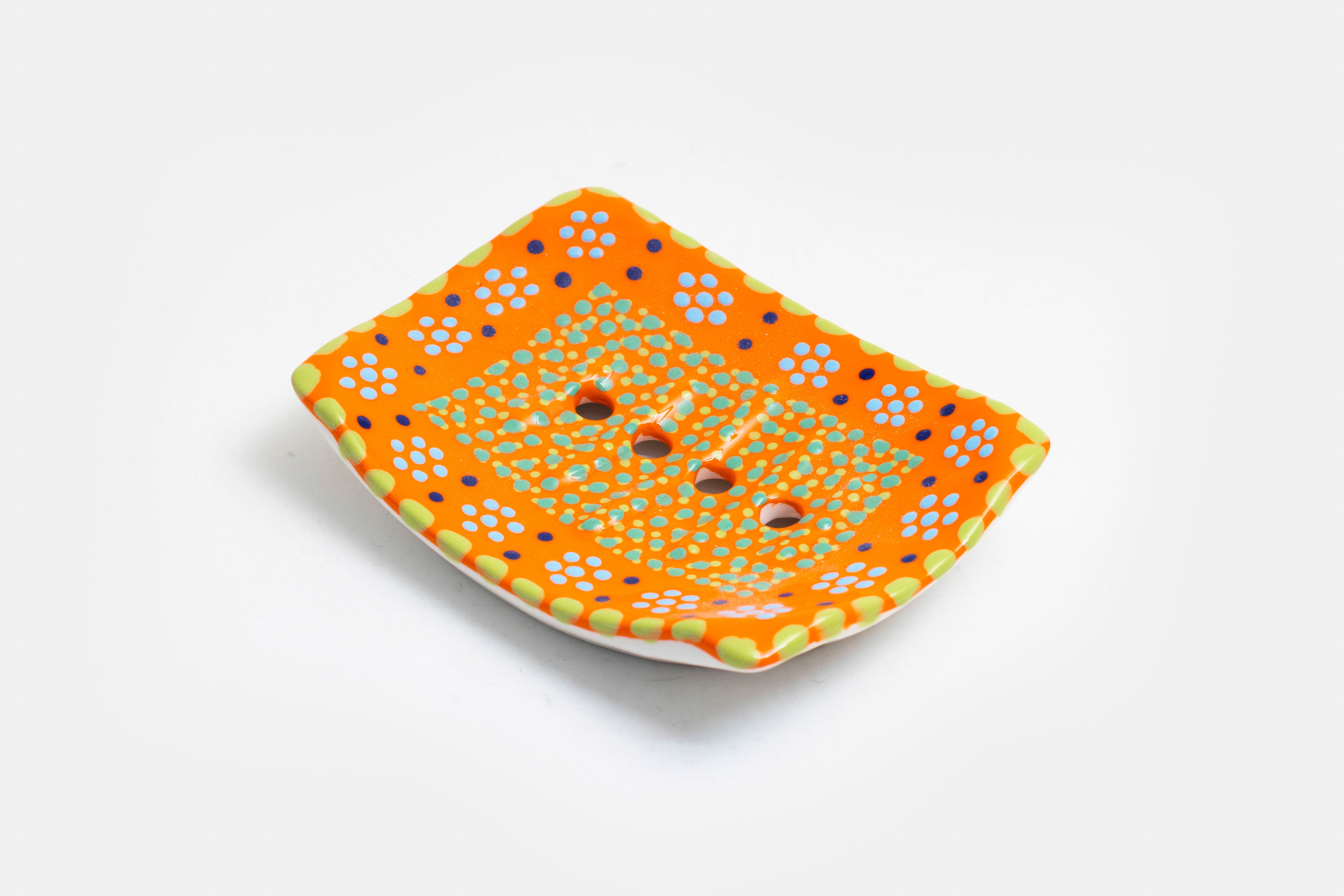 Ceramic square soap dish with base color of orange. Flowery design with dots painted on top in yellow, turquoise, red and touches of lime green. Drain holes in dish!