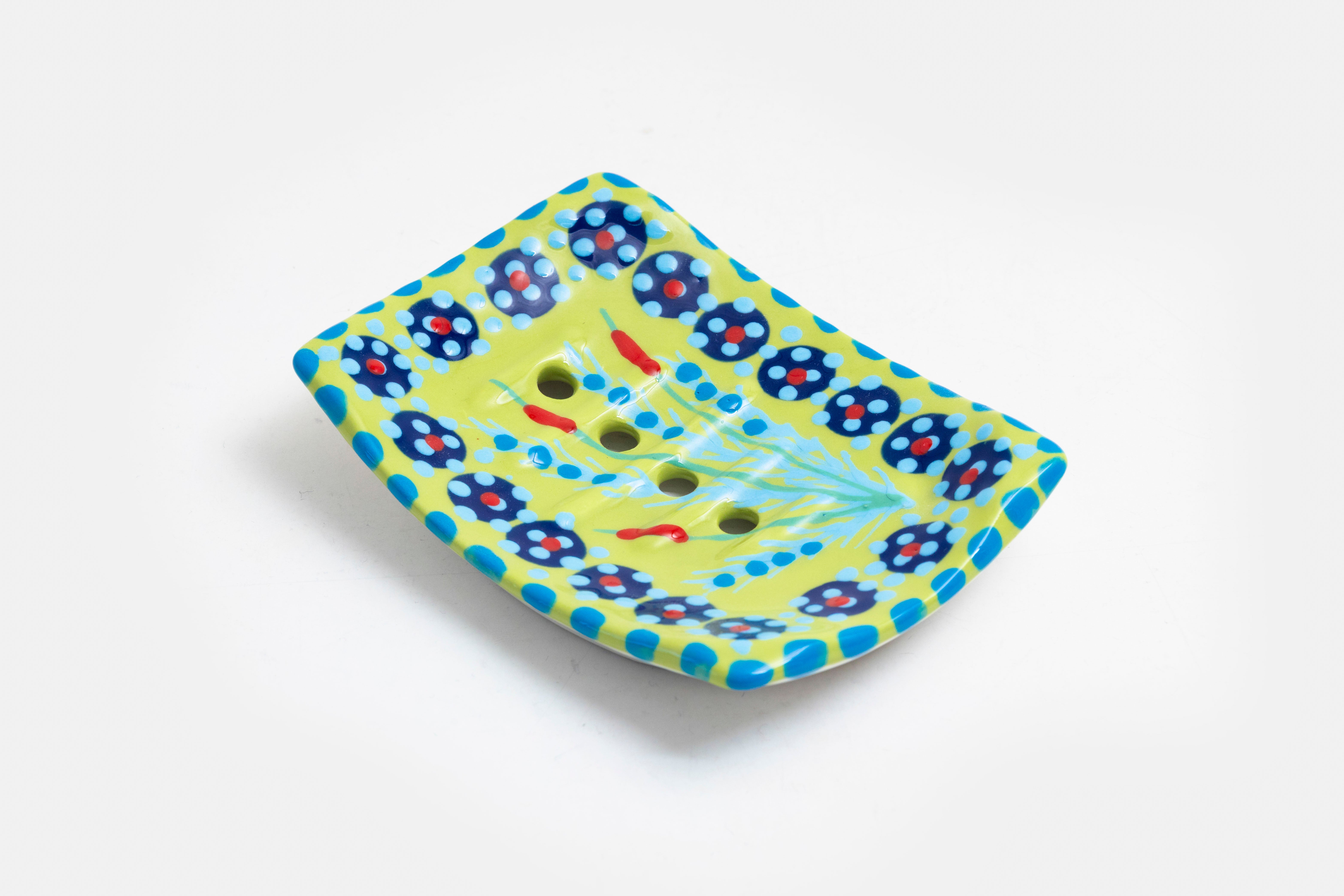 Ceramic square soap dish with base color of lime green. Flowery design with dots painted on top in indigo blue, yellow, turquoise, red and touches of orange. Drain holes in dish!