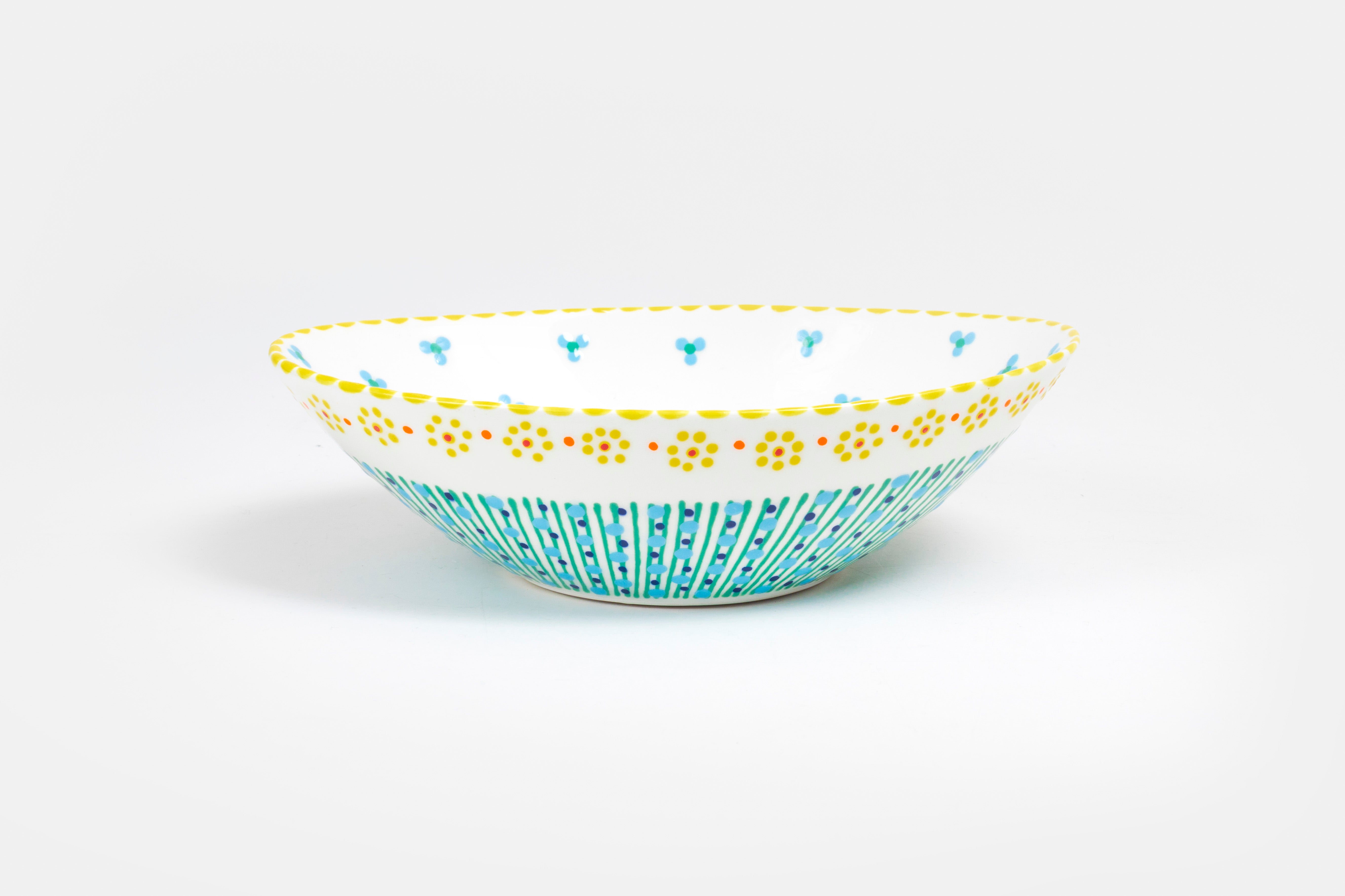 Oval ceramic serving bowl with white  base color.  Orange, yellow, indigo, baby blue, green with touches of red in dots & stripes and flowers on top. Inside is white  'dot ' flowers design. Very lovely and fairly traded!