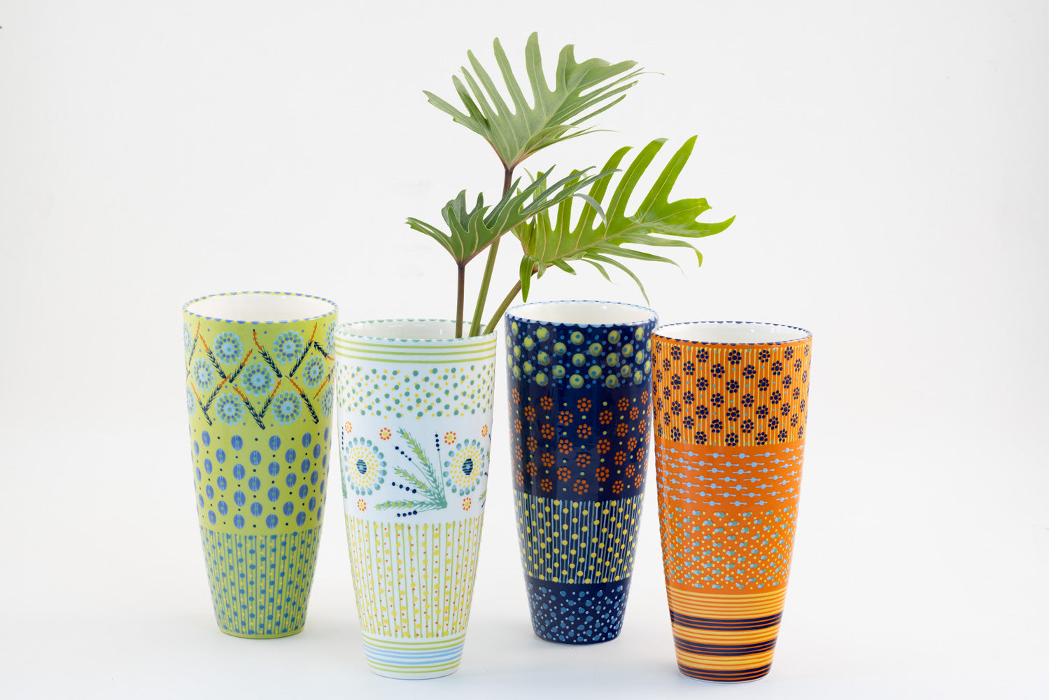 4 Classic vases with background colors of lime green, white, indigo blue, and orange.  Dots, stripe and flowers make the colorful designs on the background colors. 12" tall x 6" wide.