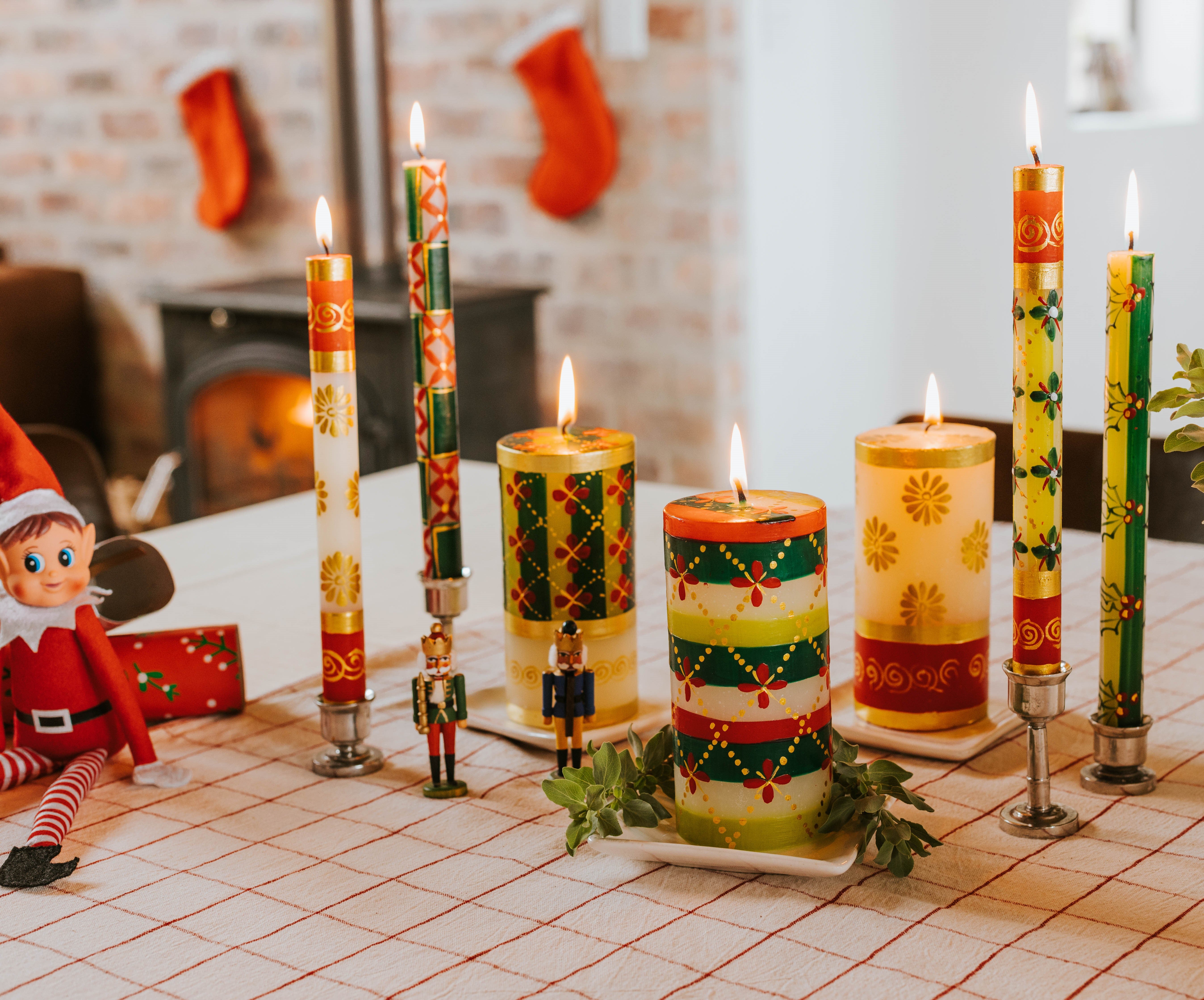 Lifestyle photo of 3 Christmas pillars & 4 dinner tapers as the centerpiece of the dinner table. Stocking are hung in background with a lovely fire glowing. So pretty!