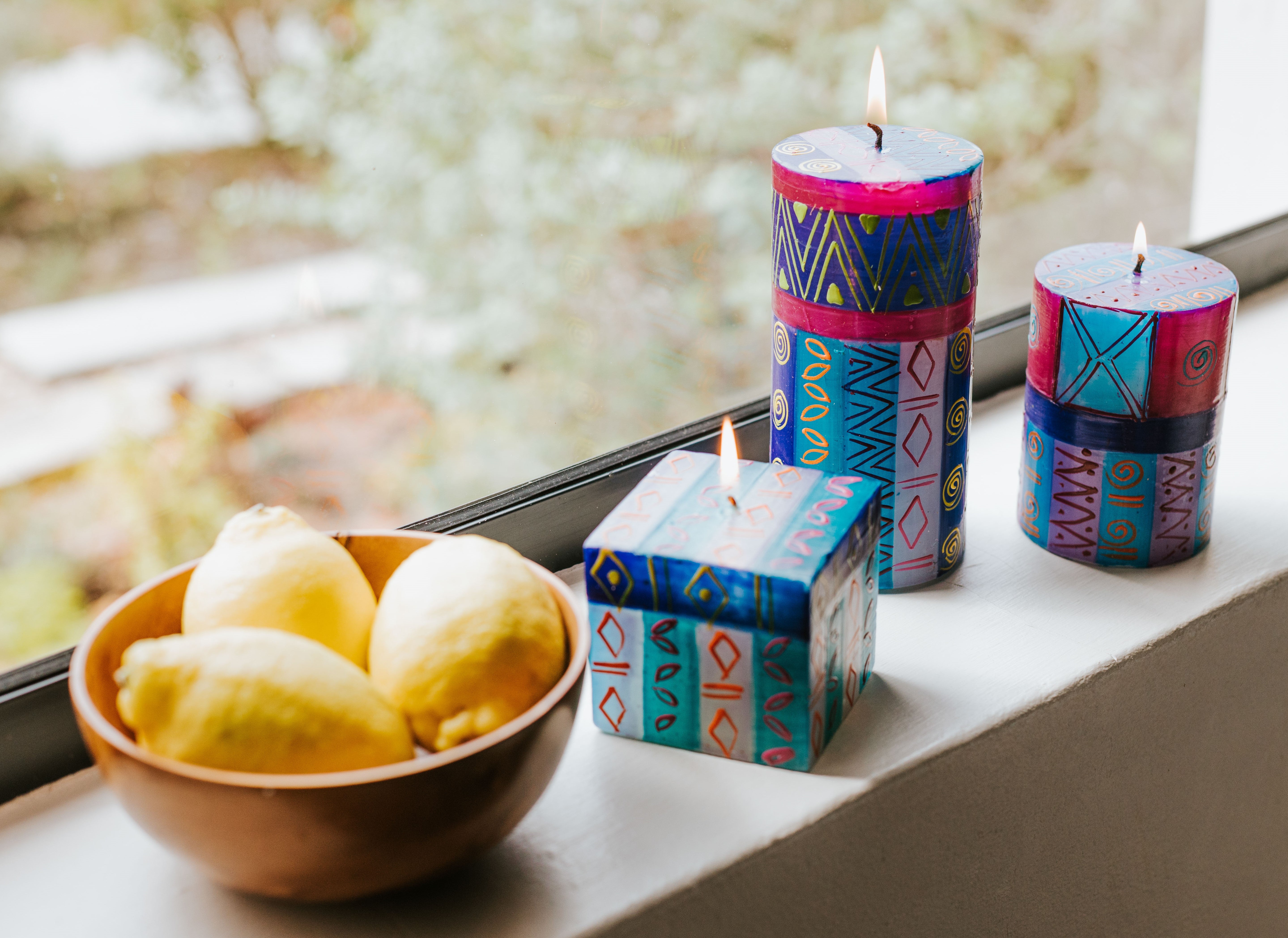 Lifestyle shot of Blue Moon 3x4 pillar, 3x6 Blue Moon pillar and 3x3x3 Blue Moon cube. Burning on a window ledge with a bowl of lemons, bringing out the touches of yellow on the candles.