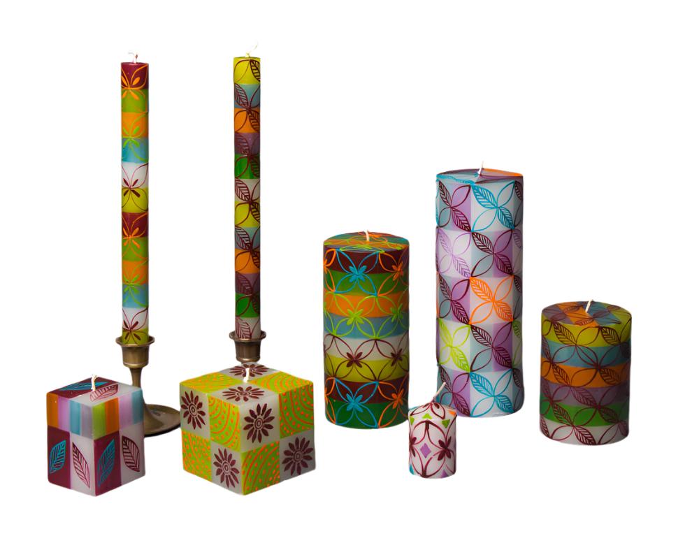 Set of 7 Magic Garden candles; taper pair, cubes, pillars, votive. White base with green, orange, turquoise, and lavender stripes. Overlay of pigment colors with a variety floral and leaf designs.