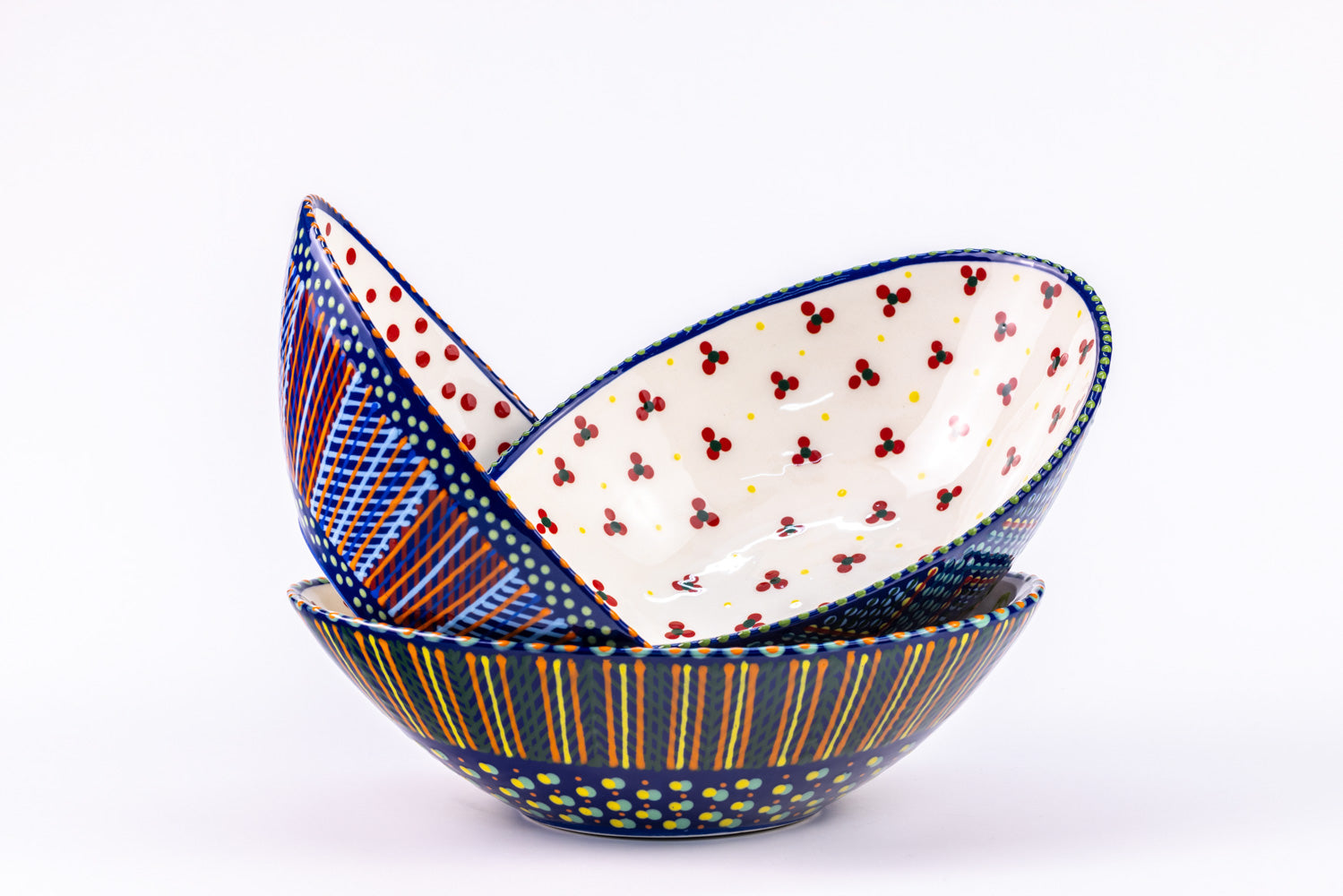 3 stacked ceramic oval serving bowls with Indigo Blue base color with dots & stripes on top in colors of red, yellow, orange, turquoise & green. Inside of one bowl is sweetly painted with red 'dot' flowers and yellow dots.