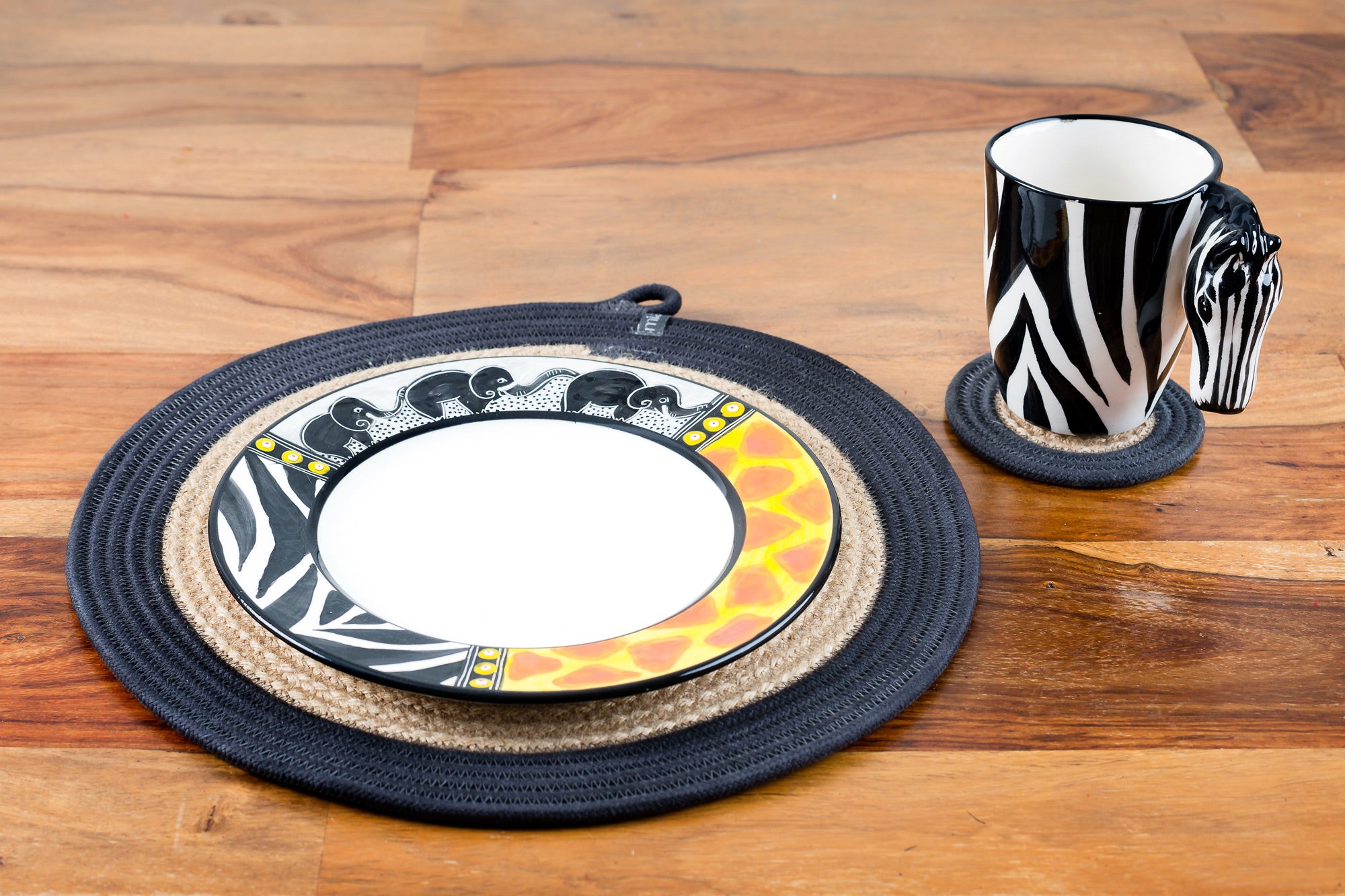 Ceramic Zebra coffee mug. White mug painted in zebra print with a zebra head for the handle! White inside.  Along side the African Animal print plate. Both on woven mats on a table.  Very cute pair as the zebra print is on both the mug & the plate.