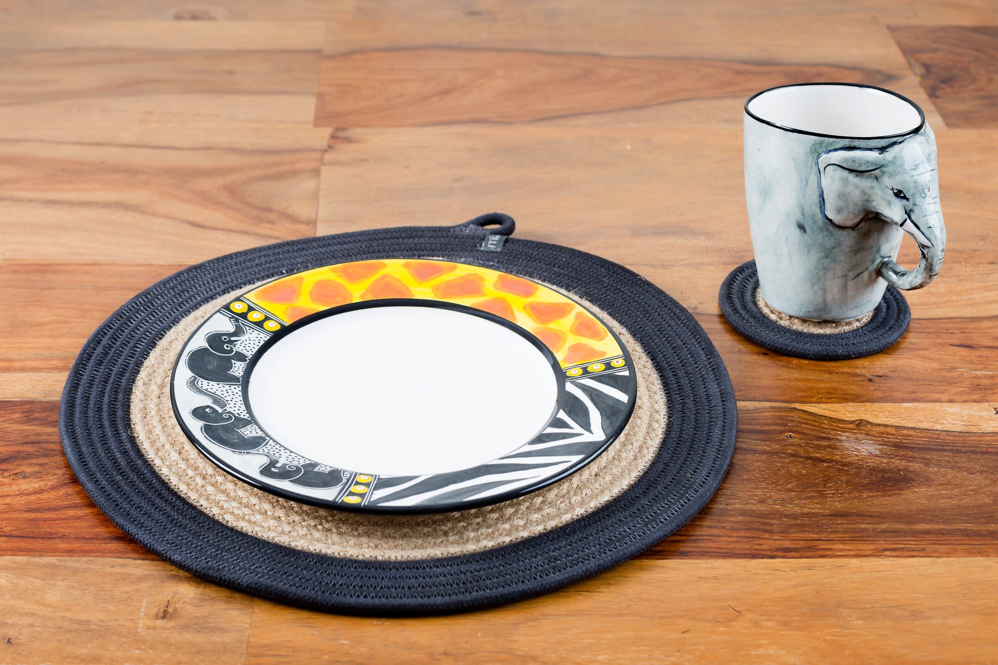 Whimsy Animal print side plate! White plate with the rim painted in zebra & giraffe print and three small elephants in a line on a woven place mat on a table.  Along side is the Elephant mug on a woven coaster. Great fun pair!