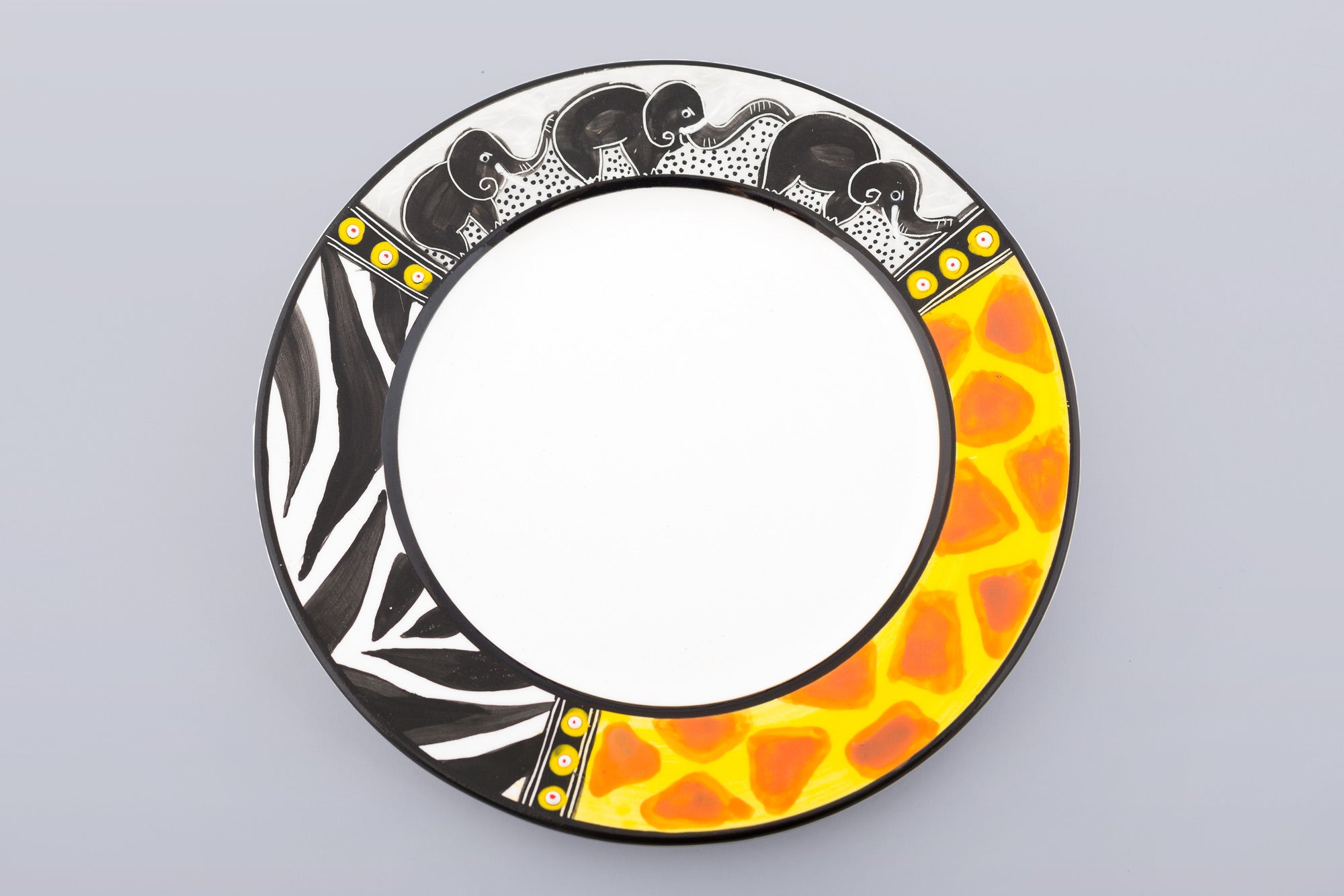 Whimsy Animal print side plate on grey background. White plate with the rim painted in zebra & giraffe print and three small elephants in a line - trunks up for Good Luck!