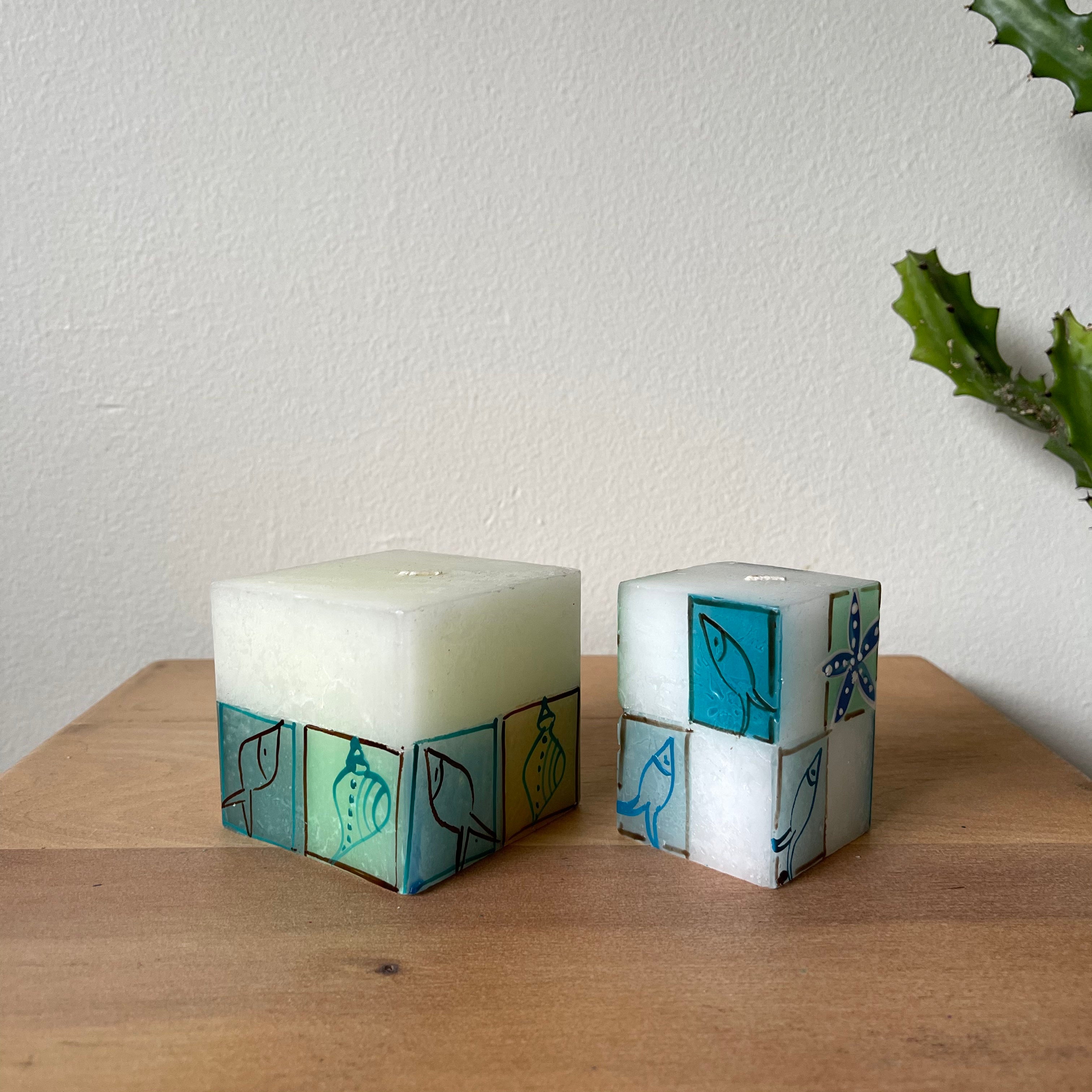 Arniston 3'x3"x3" cube candle and 2"x2"x3" cube candle.  White background with fish and sea shells painted in marine blues and green.  Fair Trade.