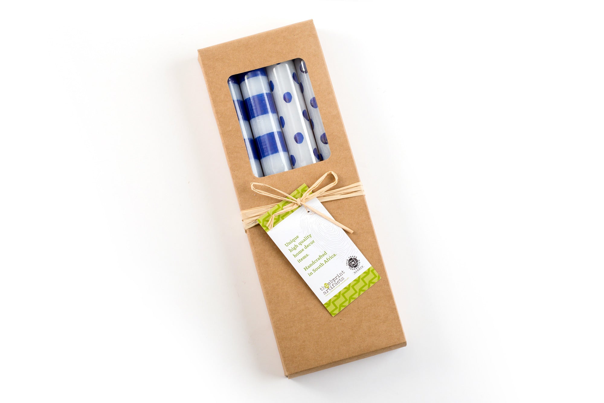 4 white tapers in a kraft gift box; two with blue dots and two with blue stripes. The gift box is tied with a story card. Fair Trade.