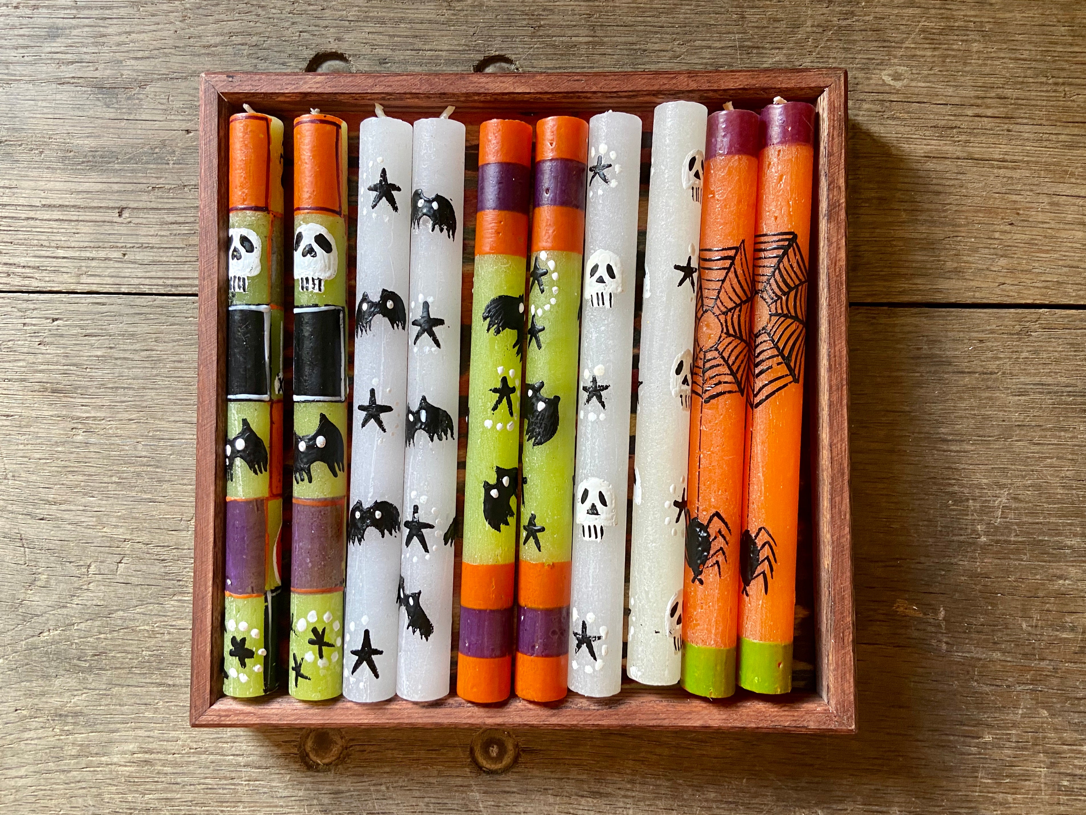 Halloween hand made & hand painted tapers candles. 5 different pairs; green background, with skulls and bats with orange & black squares, white candle with bats and black stars, green candle with orange & purple stripes with bats and black stars, white candles with skulls and black stars, orange candles with spider nest and spider crawling up the candle! 