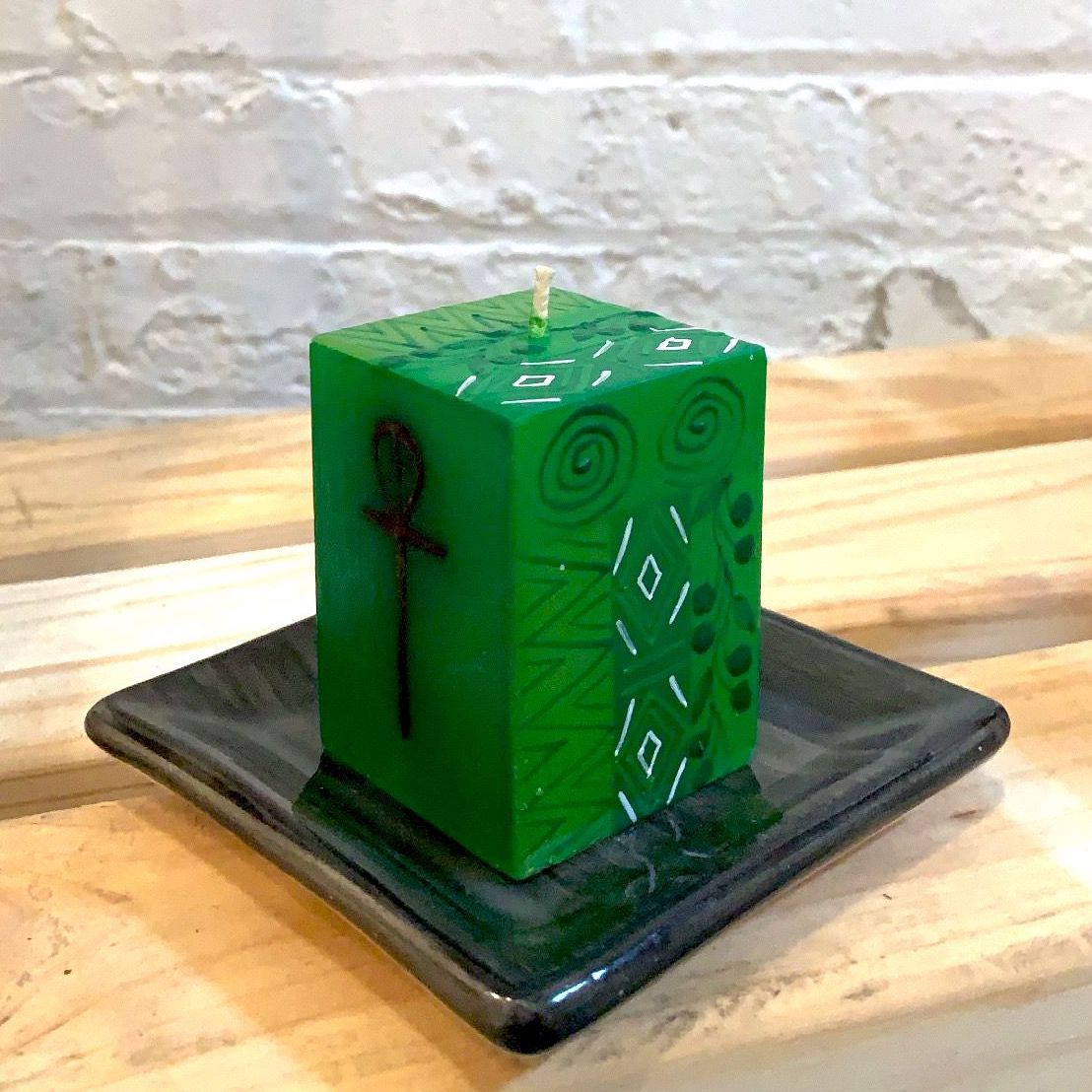 Kwanzaa green 2x2x3 cube candle showing symbol on the front and flower design down the sides.  Sitting on a black candle coaster.  