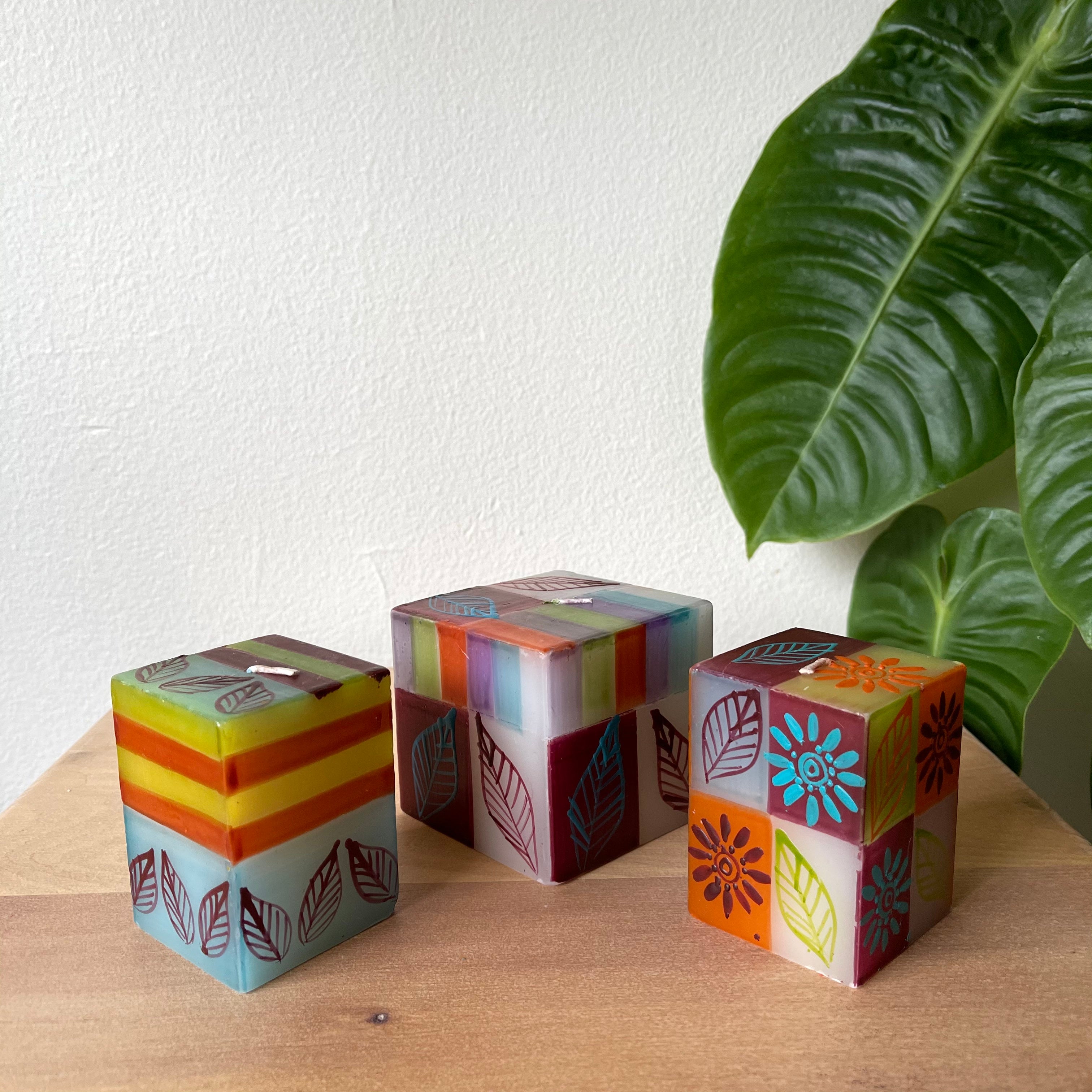 Magic Garden candle collection 2/ 2x2x3 cube candles and 1/ 3x3x3 cube candle.  Painted with a floral design in turquoise, maroon, green, yellow, and orange. Fair Trade home decor. 