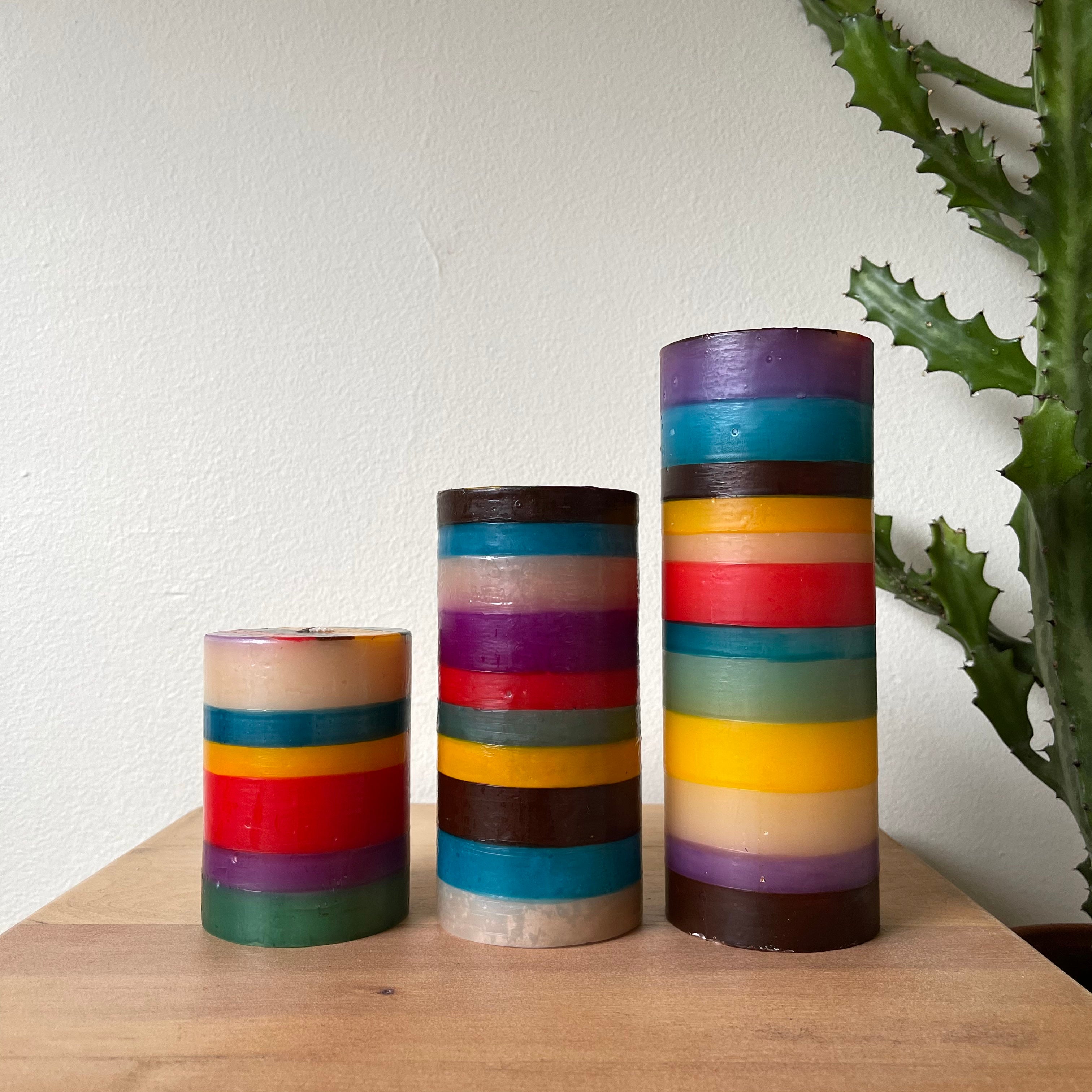 Memphis Stripe Candle collection pillar candles, 3x4 pillar candle, 3x6 pillar candle, and 3x8 pillar candle.  Painted in stripes of purple, turquoise, brown, yellow, green & red.  Fair Trade home decor.