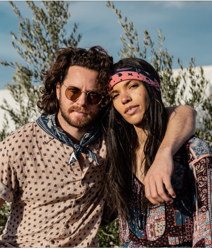 A man and a woman each wearing a bandana.  The man has it tied around his neck, and the woman has it tied around her head.  Very relaxed, showing how the bandana accents casual wear.