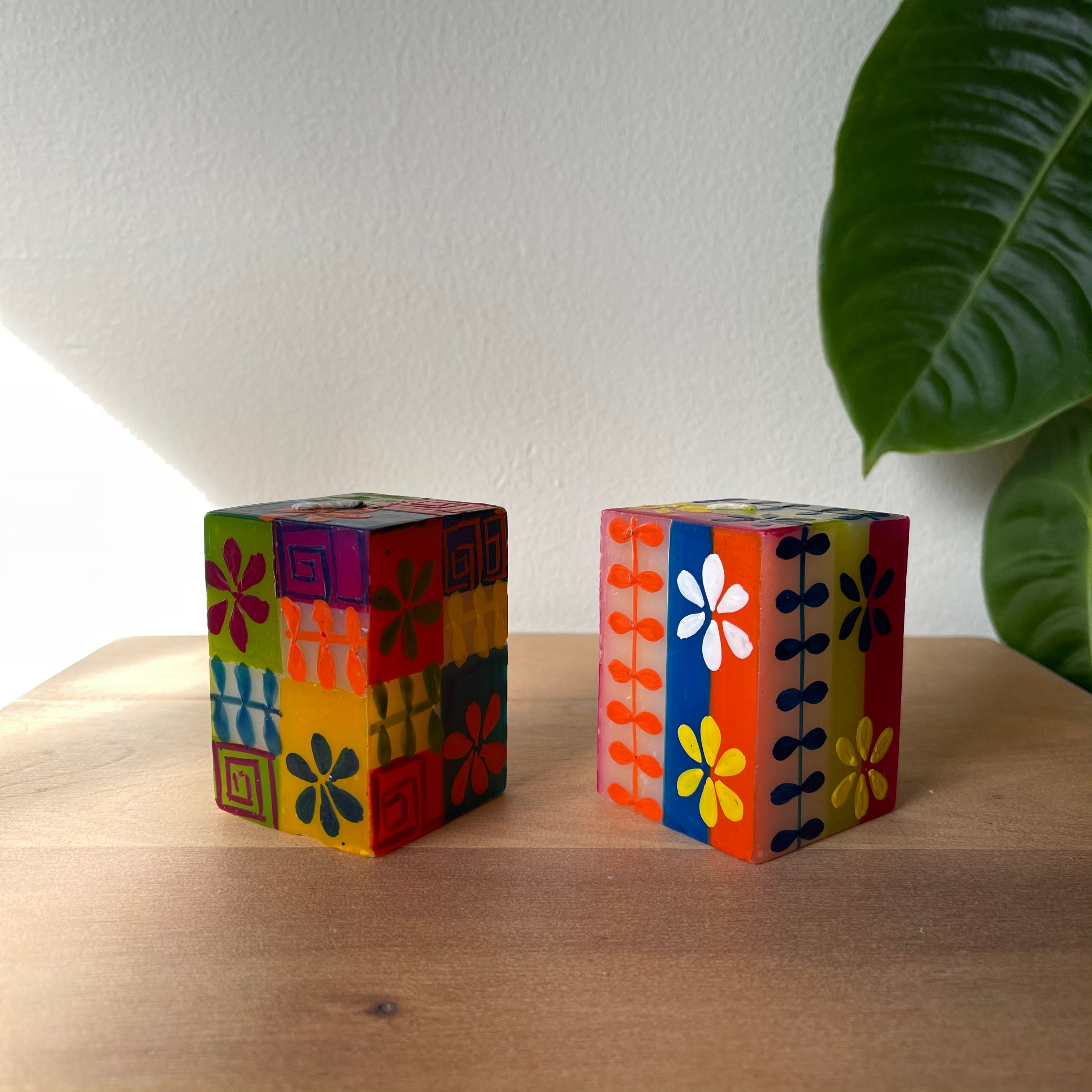 Two Summer hand painted cube candles. Colorful with a background of greens, orange, read, and blue with white summer flowers, dots & designs. 