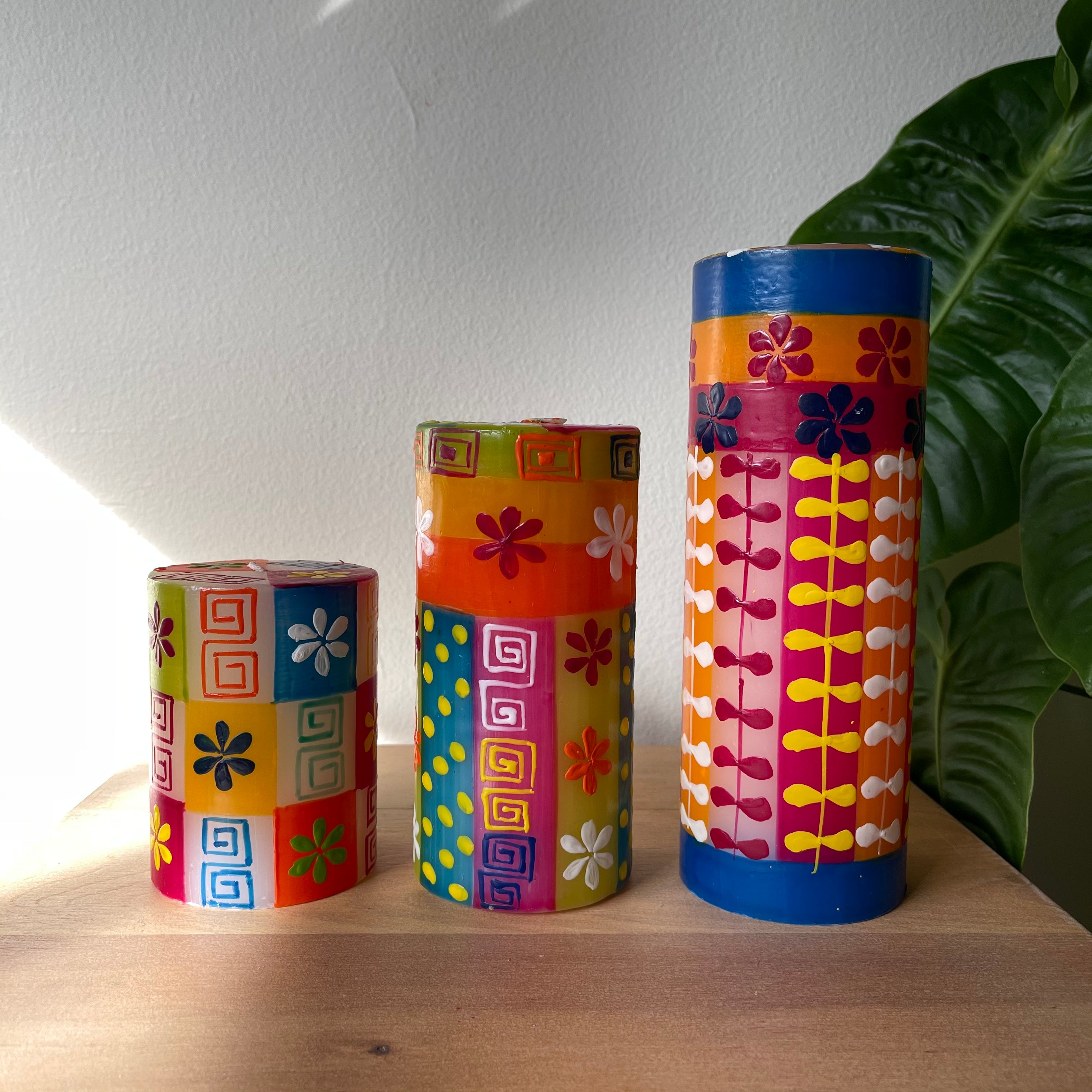 Three summer hand painted pillar candles. Colorful with a background of greens, orange, read, and blue with white summer flowers, dots & designs. 