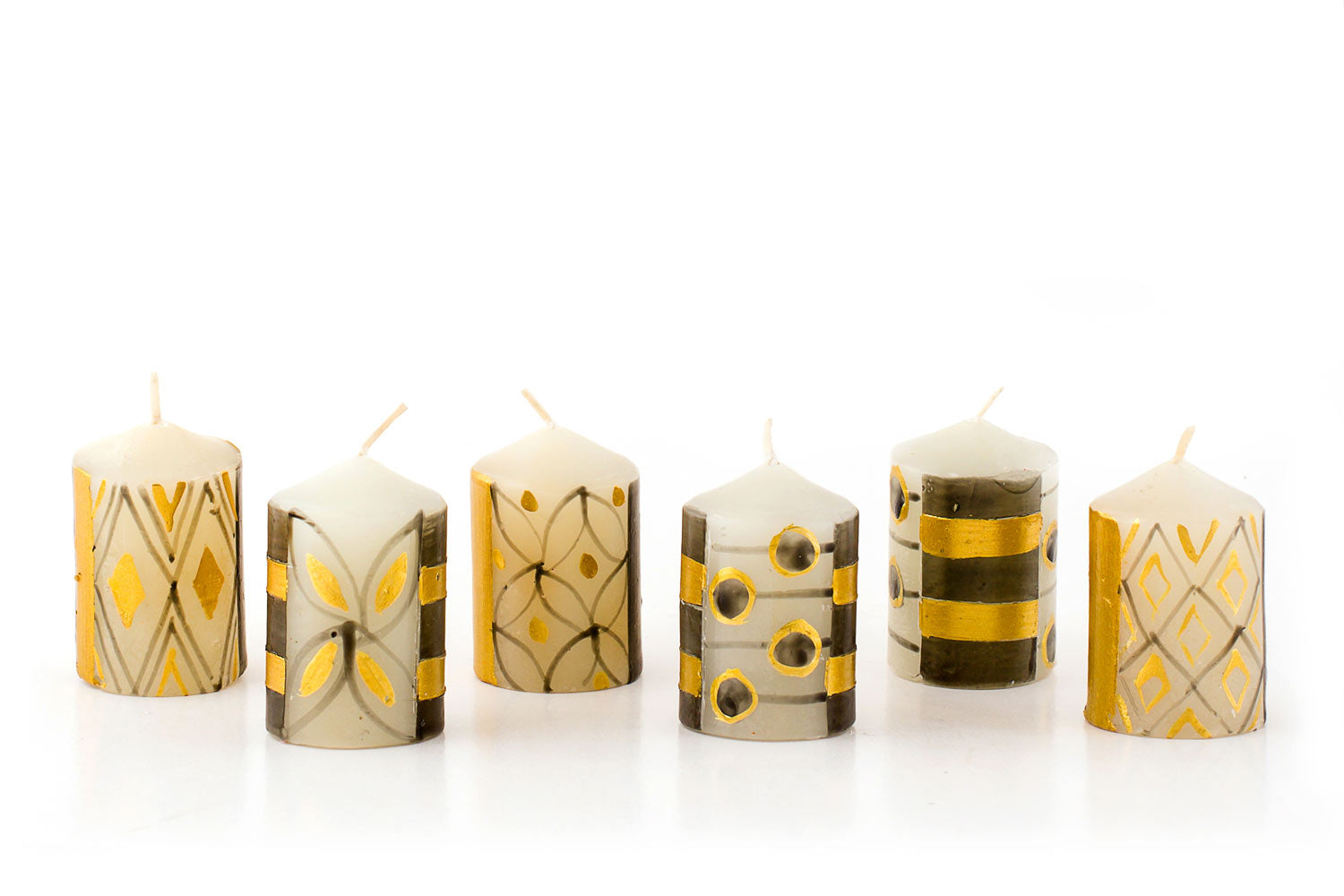 Celebration design votive candles. white background with grey/black and gold designs of stripes, dots, and floral. Fair Trade.