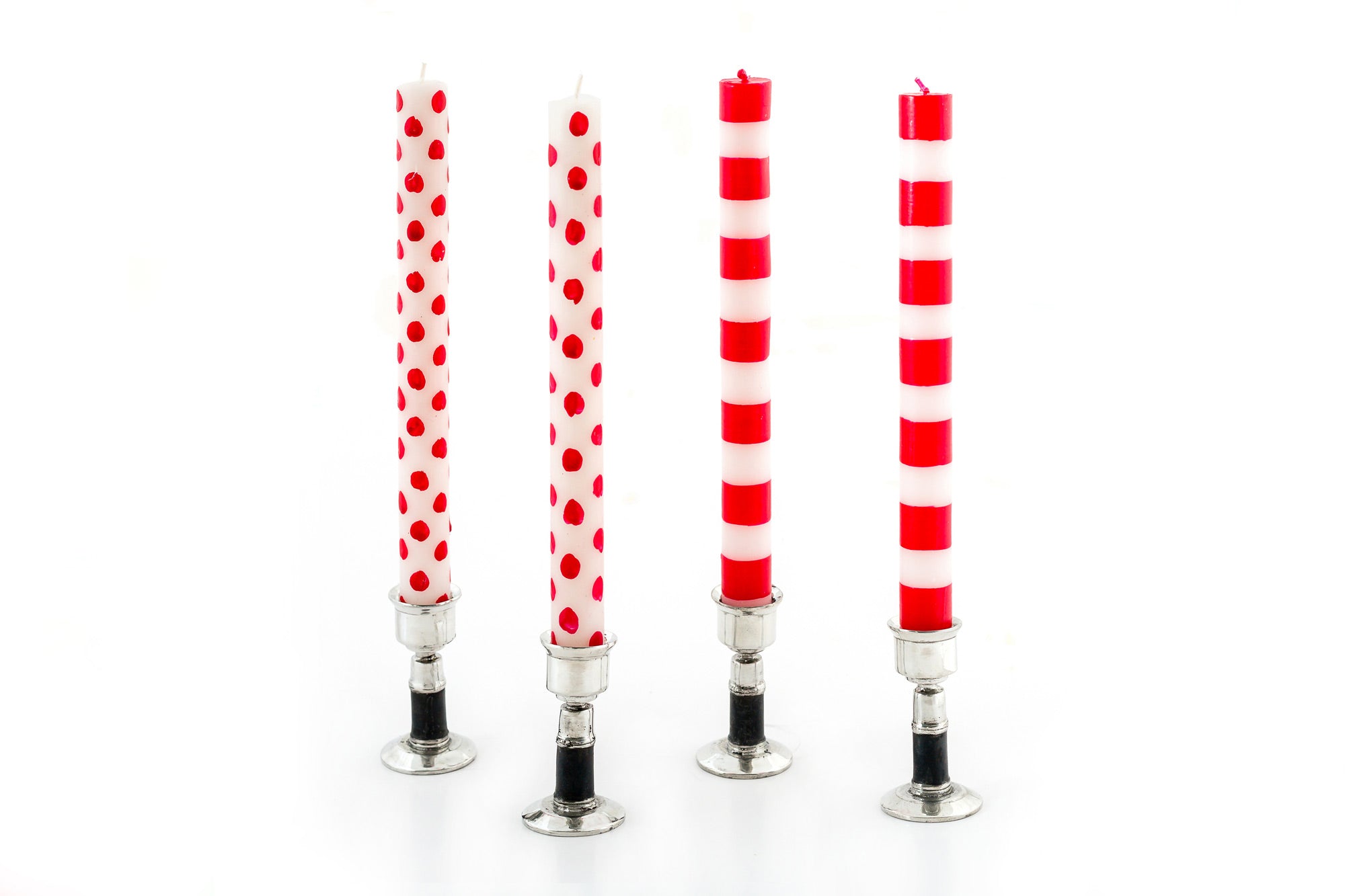 Two white taper candles with red dots alongside two white tapers with red stripes, all standing in pewter taper holders with black bands. Fair Trade products.