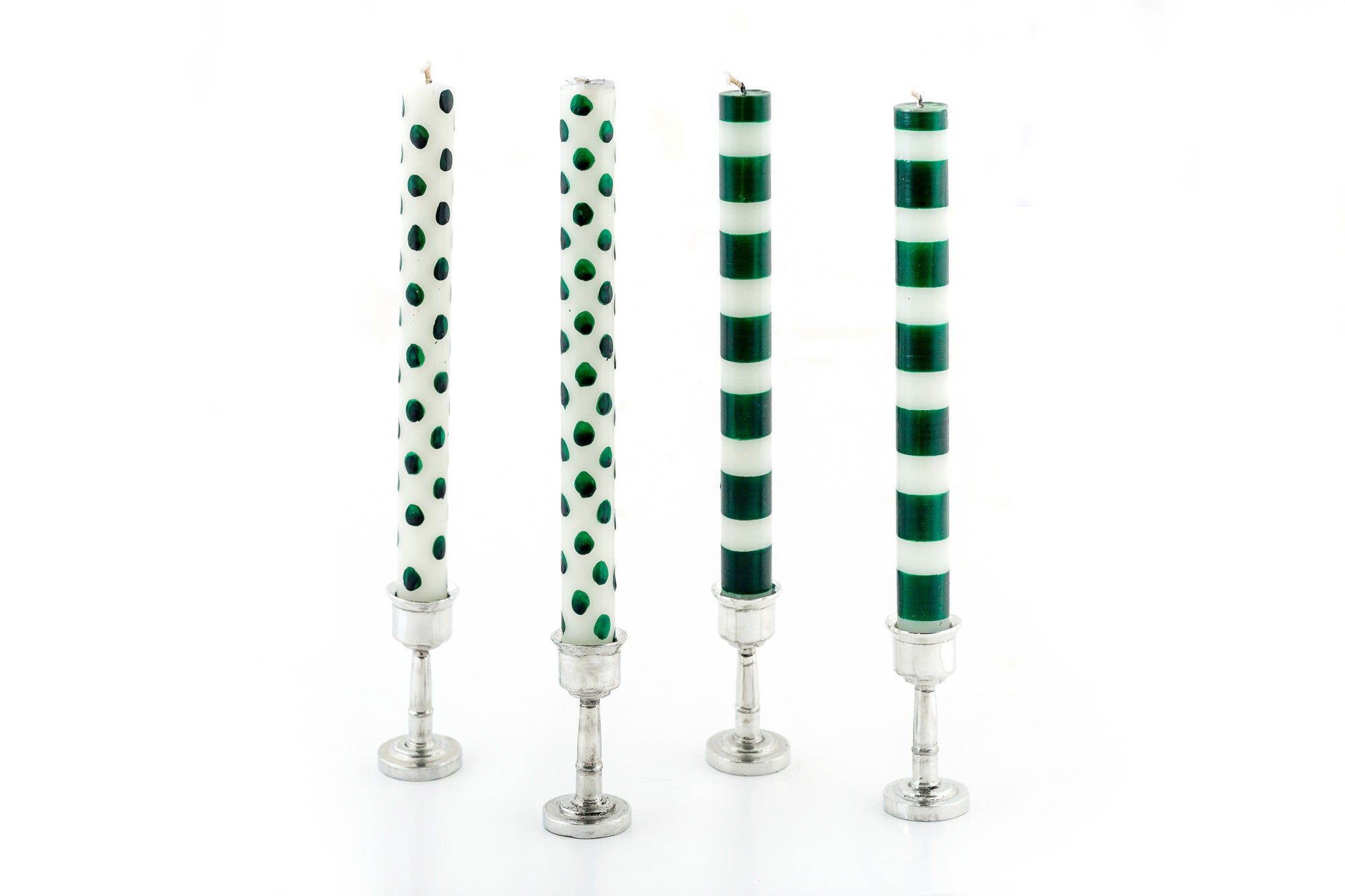 Two tapers with a white background & dark green dots alongside two tapers with white background and dark green stripes.  All four tapers are in pewter taper holders.