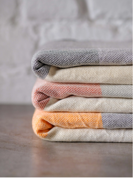 Linen blend turkish towels folded in a stack; black/grey, red/grey, and orange/grey.  All three have a cream color background.  