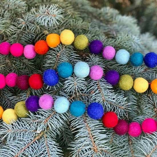 Three strings of felt garland balls in all the colors of the rainbow draped on a tree.  