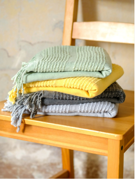 Stack of 4 stone washed Turkish towels on a wooden chair.  Light green, yellow, grey-black, and white.