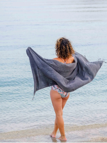 Girl on the beach using the grey-black stone washed Turkish towel as a wrap.