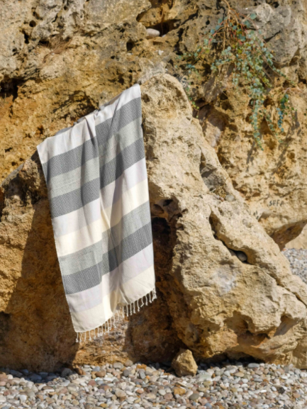 Striped Turkish Towel cream, black & grey, hanging on a rock in the sunshine.