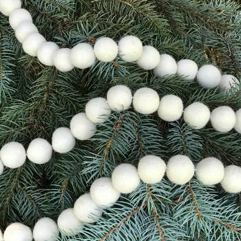 Three strands of white felt garland balls draped on a tree. 